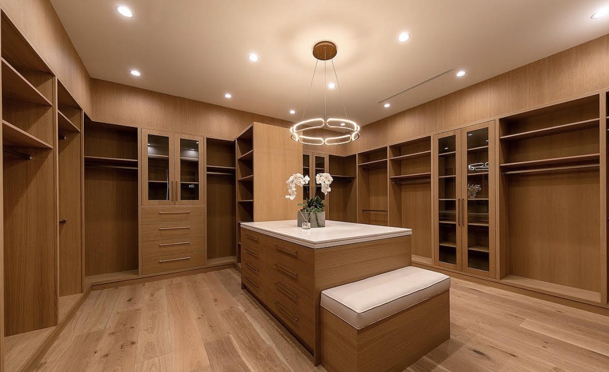 Custom master closet with built-in wood cabinetry, glass-front storage, center island, and pendant lighting.