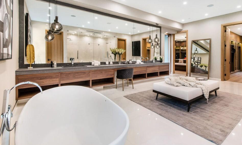 Spacious master bathroom with long double vanity, wall-to-wall mirror, pendant lights, and freestanding tub.