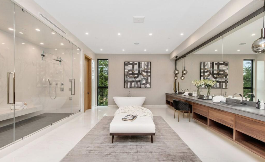 Bright spa-style bathroom with glass walk-in shower, long double vanity, freestanding tub, and bench on a rug.