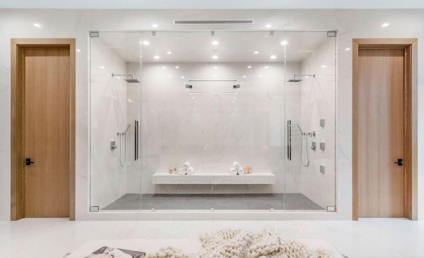 Large glass-enclosed walk-in shower with bench seating and dual showerheads in a bright white bathroom.