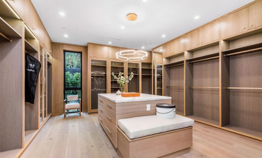 Custom walk-in closet with wood built-ins, glass cabinet doors, and a marble-topped center island.