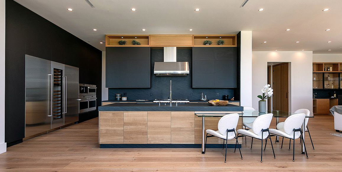 Modern kitchen with dark upper cabinets, light wood island, stainless appliances, and dining table seating.