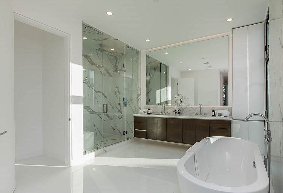 White marble bathroom with glass shower, floating double vanity, and freestanding tub.