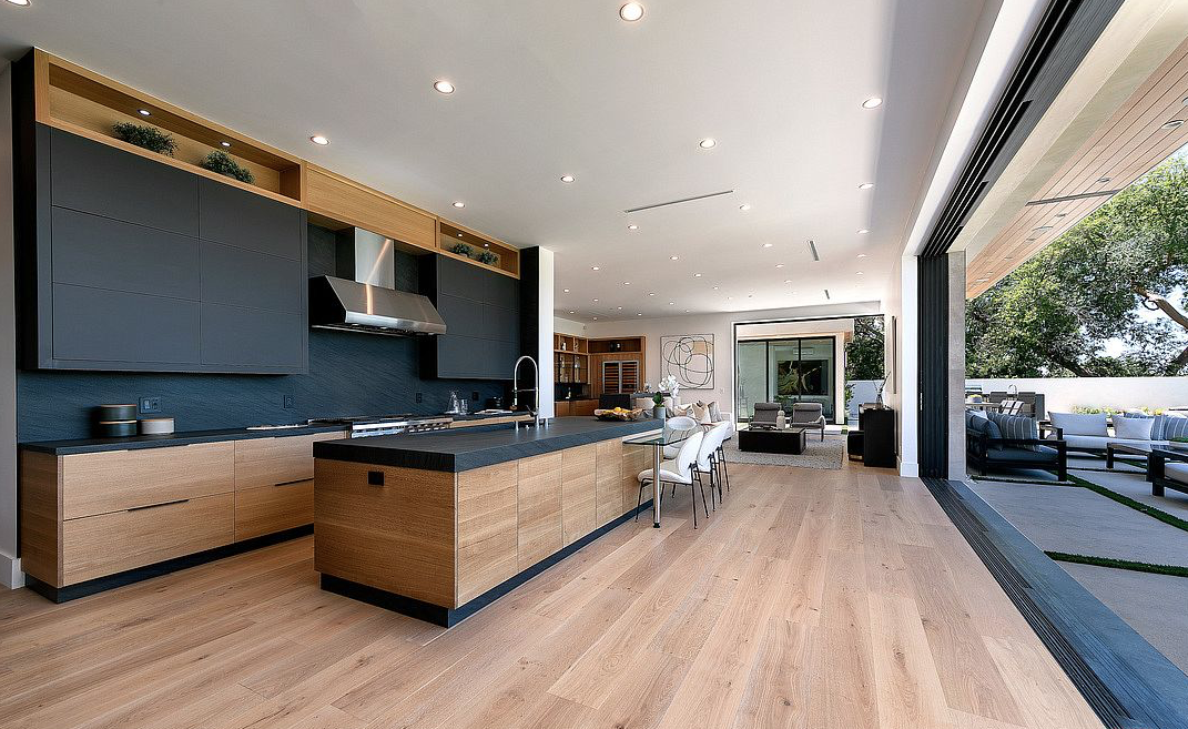 Open-concept kitchen with wood cabinetry, dark upper cabinets, large island, and sliding doors to the patio.